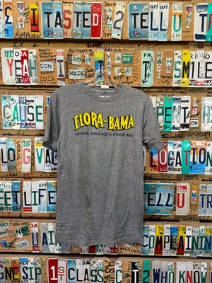 A gray Flora-Bama brand t-shirt with a wavy yellow logo on the front hanging on license plates