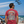 Man on a beach wearing a red t-shirt with a patriotic design, watching Blue Angels flyover.