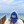 A person on a wooden boardwalk at the beach wearing a blue and white trucker hat with 'beach happy' embroidered on the front, holding the brim in front of their face.