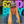 A woman with long blonde hair stands in a retail store wearing a blue t-shirt and a gray baseball cap with a '62nd Battalion' patch. Behind her are large neon signs reading '62ND BAY' in yellow, pink, and blue, with shelves of small items on a wooden wall above.