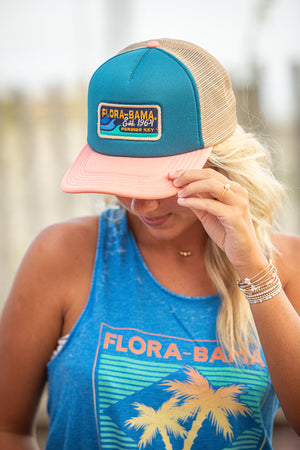 girl wearing blue and pink flora bama patch hat with a wave.
