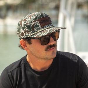 Man wearing a camouflage cap and sunglasses with a blurred background