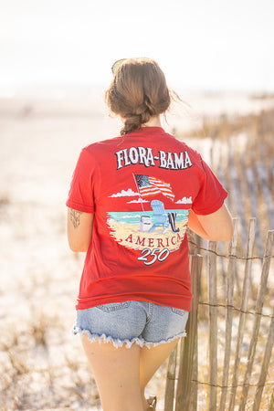 Person wearing a red 'Flora-Bama' t-shirt with beach graphics on a beach.