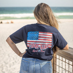 person wearing a navy blue t-shirt with a graphic of the American flag and the 'Flora-Bama' logo on it.