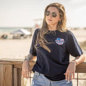 Woman wearing a black t-shirt with american flag on the left front chest and florabama logo