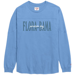 A light blue long-sleeve t-shirt with 'FLORA BAMA' printed across the chest in a dark teal block font, with 'perdido key' in white script underneath. The shirt is displayed flat against a solid white background.