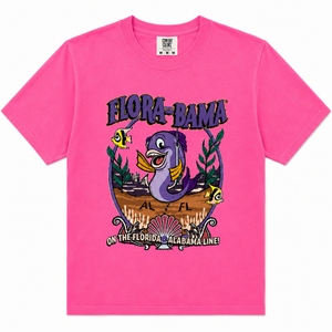 A bright pink short-sleeve crewneck t-shirt featuring a colorful graphic print on the front. The graphic displays a purple sea turtle, yellow tropical fish, and the text 'FLORA-BAMA' and 'ON THE FLORIDA - ALABAMA LINE!'.