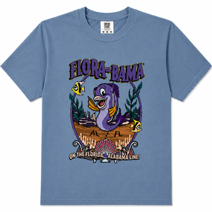 A denimshort-sleeve crewneck t-shirt featuring a colorful graphic print on the front. The graphic displays a purple sea turtle, yellow tropical fish, and the text 'FLORA-BAMA' and 'ON THE FLORIDA - ALABAMA LINE!'.