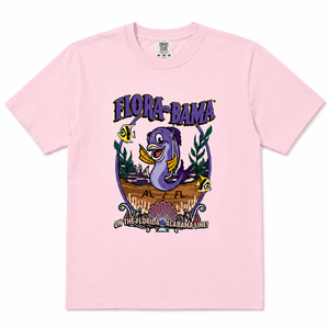 A pink short-sleeve crewneck t-shirt featuring a colorful graphic print on the front. The graphic displays a purple sea turtle, yellow tropical fish, and the text 'FLORA-BAMA' and 'ON THE FLORIDA - ALABAMA LINE!'.