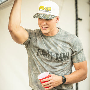 Man wearing a 'Flora-Bama' camo tshirt with black flora bama logo, white flora bama hat with camo bill and yellow logo