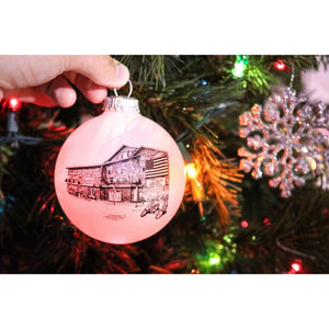 image of hand hanging ornament on christmas tree, white ornament with new florabama building sketch