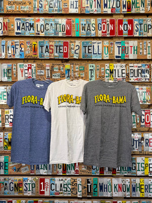 three shirts - A gray, white and blue Flora-Bama brand t-shirt with a wavy yellow logo on the front.