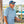Man wearing a blue patterned shirt, cap, and sunglasses by a dock with boats in the background.