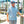 Man standing on a dock wearing a blue patterned shirt and sunglasses, with boats in the background.