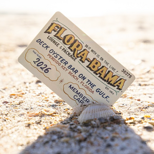 flora bama membership card propped on a shell in the sand