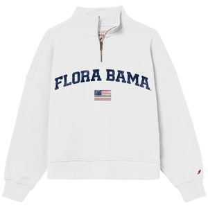 A white quarter-zip sweatshirt featuring 'FLORA BAMA' printed in navy blue arched letters across the chest, with a small American flag graphic underneath. The image is shot against a clean white background.