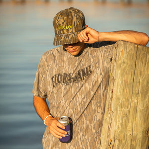 Person wearing a camouflage hat with yellow florabama logo and camouflage shirt with flora bama black logo