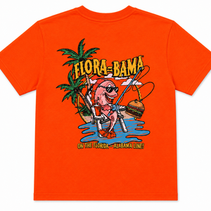 Bright orange short-sleeve t-shirt with a colorful cartoon graphic on the front featuring a pink character, palm trees, the text 'FLORA BAMA', and blue water, shown on a plain white background.