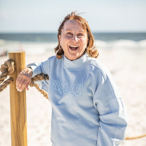 Person wearing a light blue sweatshirt with text on a beach