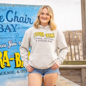 Woman wearing a gray hoodie with 'Flora-Bama' branding in front of a Blue Chair Bay sign.