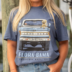 Person wearing a blue t-shirt with a graphic of a truck, dog and 'Flora-Bama' text.