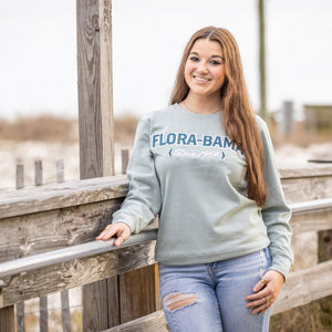 Woman wearing a 'Flora-Bama' green sweatshirt standing on a wooden boardwalk.